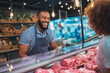 © Maksym - Butcher serving customer at meat counter in modern grocery store