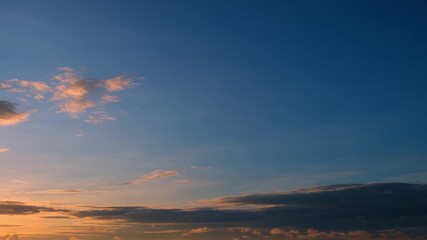 Wall Mural - A time-lapse video captures a sunset sky with scattered clouds glowing in warm orange hues, contrasting against the darkening blue sky, showcasing a serene and peaceful transition from day to night.
