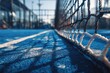 © Aisyah - Close-up of a vibrant blue padel court,  net and lines.  Sunlight casts shadows on the surface