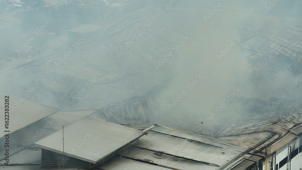 Industrial fire spreads smoke over large factory rooftops, seen from ...