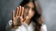 © Ketanoff - In a calm indoor environment, a woman raises her hand to signal stop as she addresses harassment, visibly expressing defiance and courage against inappropriate behavior