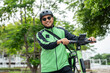 © Chanakon - Rider food delivery man wearing green uniform and helmet ride the EV scooter delivery food service to customer. Happy delivery man with green backpack shipping of goods to customers by scooter