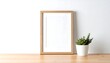 © PANGERAN - A modern blank wood frame mockup with a succulent plant on a light wooden surface, White wall mockup frame and small houseplant,  a great image to illustrate decoration ideas