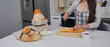 © Imageologist - A person in a checkered apron slices a baguette on a wooden cutting board, with various bread bags and a plate of butter nearby. This highlights home baking and fresh food preparation