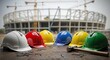 © Fajar - Construction Site Safety Equipment: Colorful Hard Hats and Tools at a Building Site, Teamwork and Safety: Protective Hard Hats, Hammer, and Nails on a Construction Project