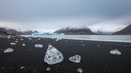 Wall Mural - glacial ice chunks scattered on a dark sandy shoreline by a frozen lagoon.