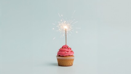 Wall Mural - party cupcake with a glowing sparkler set on a light blue surface. greeting card