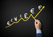 © Creative Creating - Hand drawing an upward trend line with various currency symbols on a chalkboard. Represents global finance, currency growth, and economic trends.