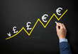 © Creative Creating - Hand drawing an upward trend line with various currency symbols on a chalkboard. Represents global finance, currency growth, and economic trends.