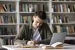 © fizkes - Productive self studying. Smiling diligent male high school student write creative academic work prepare for test exam conduct scientific research reviewing printed books digital literature via laptop