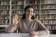 © fizkes - Remote lesson start. Smiling zoomer student girl in headset sit at desk wave hand to web camera greet teacher groupmates at beginning of virtual education event videocall consultation. Webcam portrait