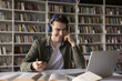 © fizkes - Hybrid learning tools. Smart smiling gen z male high school student sit in earphones before notebook look at screen attend virtual lecture webinar video call consultation prepare to take paper notes