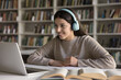 © fizkes - Digital learner. Interested smiling teen girl remote learning student wear wireless headphones study for exam in library watch education content on notebook attend online lecture ready to take notes