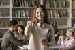 © fizkes - You can do it too. Happy gen z female student with books phone look at camera show thumb up recommend online education app promote learning course give positive feedback on high school study program