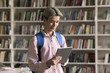 © fizkes - Digital learning tools. Smiling teen male high school student work on digital pad in modern library use mobile access to study resources navigate online materials browse information focused on screen