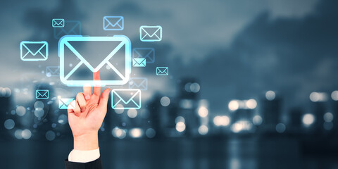 Business hand touching digital email icon on futuristic screen with glowing envelope symbols over city night background, representing communication network.