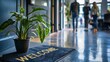 © Arslan - Welcome mat and plant in modern office interior with blurred people walking