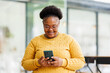 © David - Happy attractive African American business lady using Internet technology for job in co-working space, sitting at laptop, holding mobile phone.