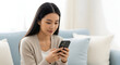 © Inkreatif - Young Asian woman using smartphone at home relaxing on comfy couch modern lifestyle technology