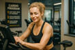 © Dmitriy - Smiling woman winking while working out on exercise bike in modern gym.