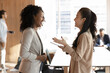 © fizkes - Friendly work atmosphere. Young multiracial businesswomen colleagues laugh talk chat in modern office share professional success celebrate teamwork discuss career achievements in casual conversation