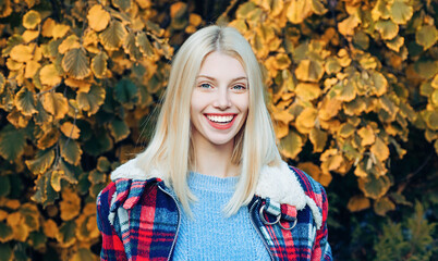Wall Mural - Autumn face of happy young woman. Smiling woman on autumn fall background. Beauty girl with fall leaves. Autumn model with fall maple leaf. Autumn portrait of beautiful happy girl.