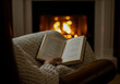 © OneAhmad - A person is relaxing on a cozy chair, reading a book with a knit blanket draped over their lap and a warm fireplace in the background