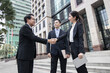 © khwanchai - Business investors in suits stand shaking hands outside a building after successful negotiations.