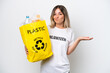 © luismolinero - Young Rumanian woman holding a recycling bag full of plastic to recycle isolated on white background making doubts gesture while lifting the shoulders