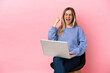 © luismolinero - Young woman sitting on a chair with laptop over isolated pink background celebrating a victory