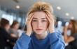 © Naila - A young woman in an office is sitting at her desk, holding her head
