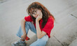 © olezzo - Portrait of a beautiful latino brunette in a red t-shirt and glasses sitting on the steps in a summer city