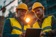 © Fatima Sial - Construction Team Collaboration: Two construction workers in reflective vests and hard hats analyze a digital tablet against the backdrop of a construction site.