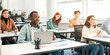 © Prostock-studio - Education, Technology, Lifestyle And People Concept. Group of diverse international students sitting at desk in classroom using laptop computers, studying and listening to teacher, writing in notepads