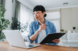 © Miljan Živković - Asian freelancer woman working from home taking notes on documents
