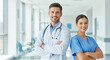 © Kaluya Stock - Smiling male doctor in a white coat and a female nurse in scrubs pose with arms crossed in a bright, modern hospital hallway