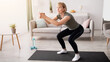 © Prostock-studio - Positive senior lady doing squats on domestic workout in living room, free space. Fit mature woman leading active lifestyle, losing weight, staying in good shape at home during coronavirus quarantine
