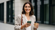 © Siti - Confident businesswoman smiling city street holding phone coffee break success professional career job urban modern lifestyle happy employee commute