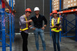 © winnievinzence - Team of three warehouse workers in hard hats and safety vests discussing a project. Represents industrial management, teamwork, and logistics planning