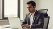 © Tida - Businessman Working on Laptop in Office - A focused businessman sits at his desk, diligently working on his laptop. He is dressed in a sharp suit, showcasing professionalism and concentration