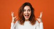 © Nuraya - Young woman expresses extreme joy and excitement with wide eyes and open mouth against a vibrant orange background