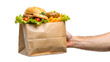 © SUHEL AHMED - Hand holding a paper bag full of fast food including a burger, french fries, lettuce, and tomatoes, isolated on transparent background