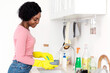 © Prostock-studio - Joyful black lady housewife washing dishes and smiling, wearing colorful rubber gloves, using sponge, copy space. Young african american woman house-keeper or made cleaning house