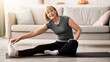 © Prostock-studio - Domestic workout. Cheerful senior lady stretching her leg on sports mat in living room, empty space. Flexible mature woman doing exercises, leading healthy lifestyle during covid lockdown