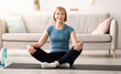 © Prostock-studio - Positive senior woman sitting in lotus pose on sports mat, meditating at home, copy space. Balanced mature lady practicing yoga, finding inner peace and mindfulness