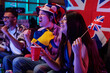 © pressmaster - Group of young adult multiethnic friends cheering and celebrating while watching sports event indoors, smiling and holding British flags, showing excitement and unity