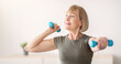 © Prostock-studio - Domestic sports training. Positive senior woman doing exercises with dumbbells, strengthening her body at home. Fit mature lady working on her biceps muscles, staying healthy during covid quarantine