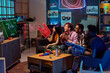 © pressmaster - Group of young adult multiethnic friends sitting on couch watching football game on television, holding foam fingers and football, cheering and reacting to action on screen