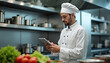 © Vadym - Pro chef in clean white uniform uses tablet, checks recipes in contemporary kitchen. Fresh produce arranged neatly beside workstation. Focus on culinary skill, technology, and food preparation.