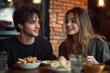 © k - Young man and woman enjoying a meal together at a cozy restaurant with warm lighting and exposed brick walls expressing friendly and happy emotions